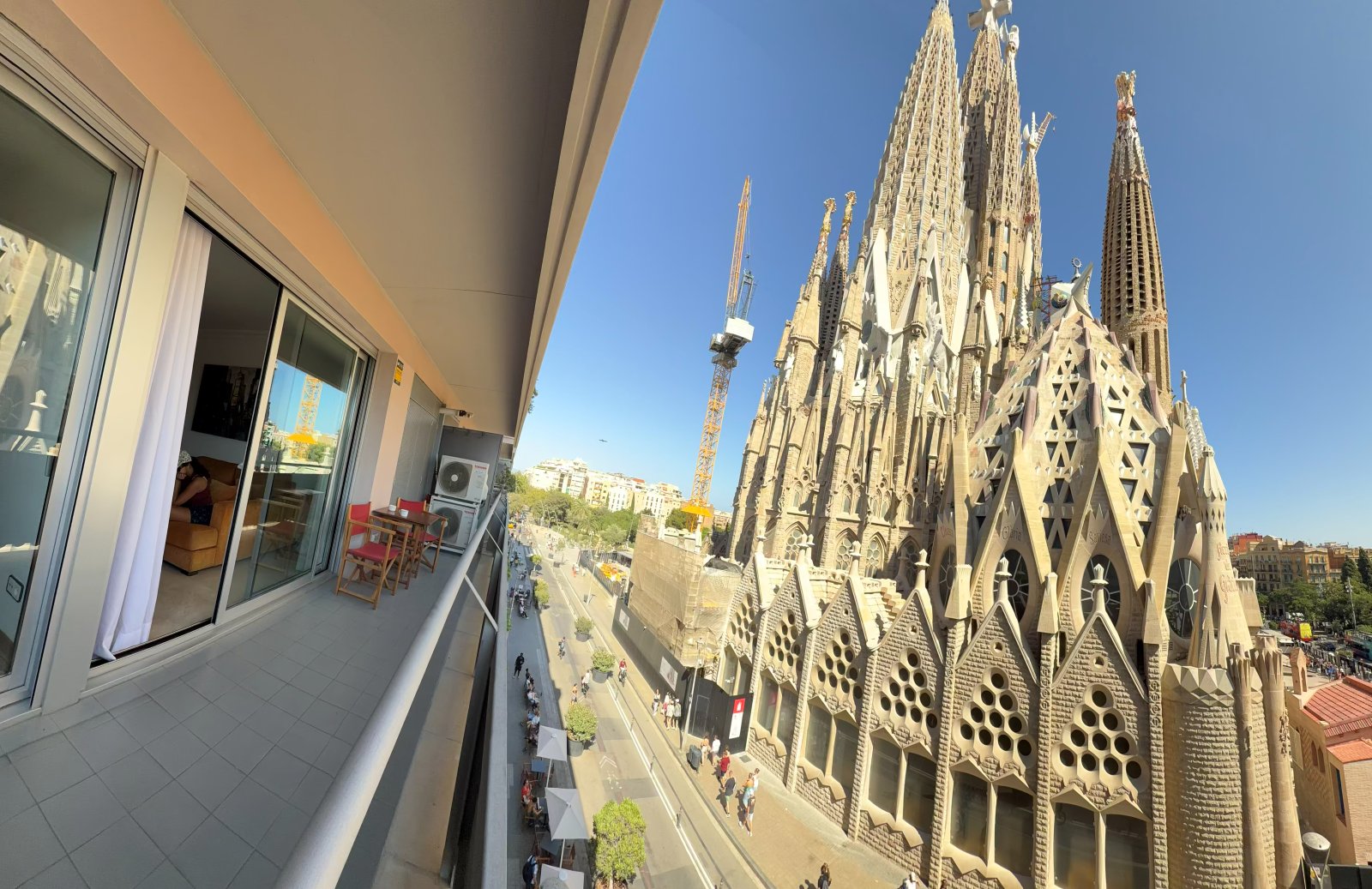 Long apartment balcony leading to a full view of the Sagrada Familia spires against a blue sky