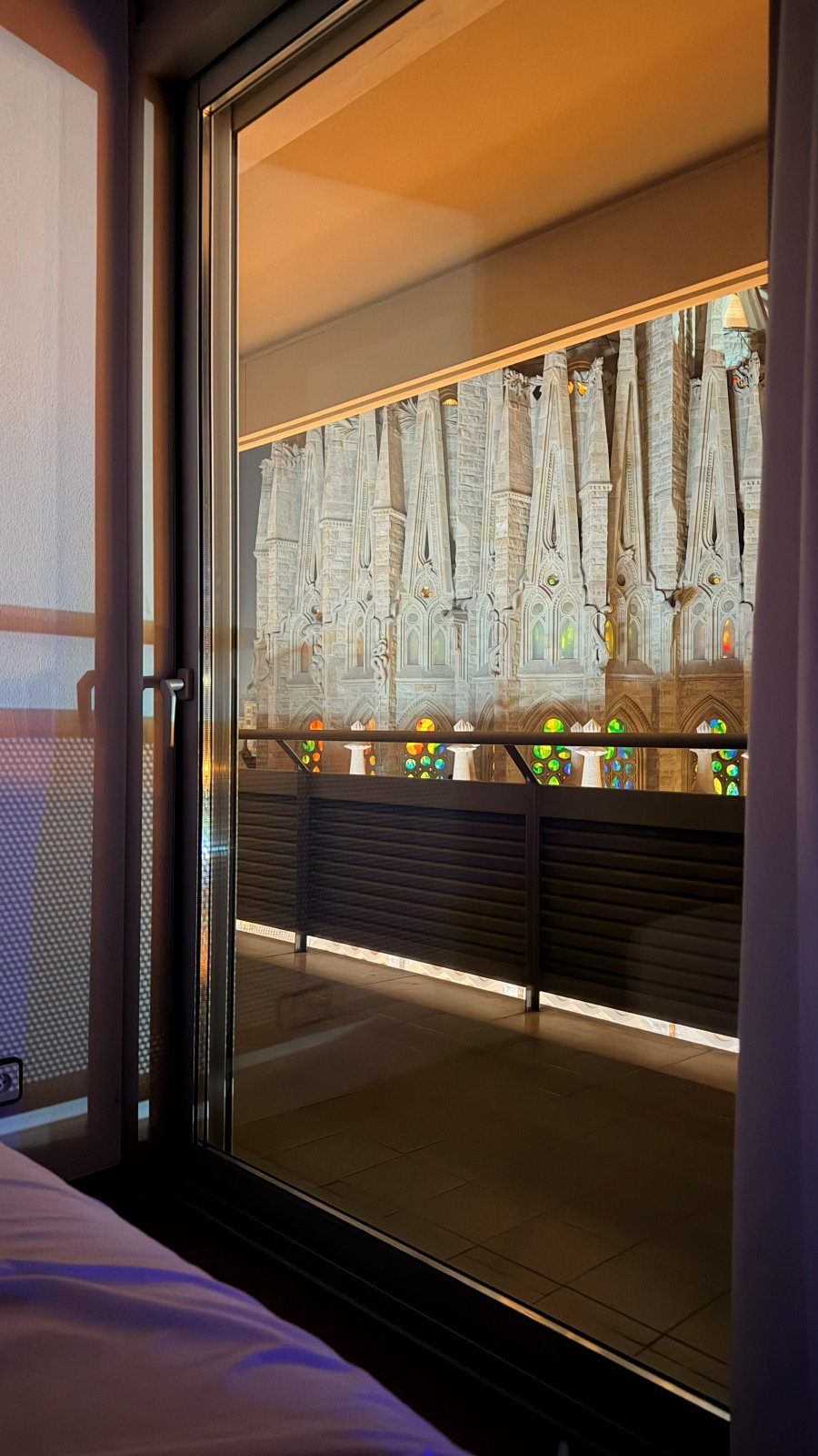 View from the bed toward the Sagrada Familia at golden hour through the balcony door