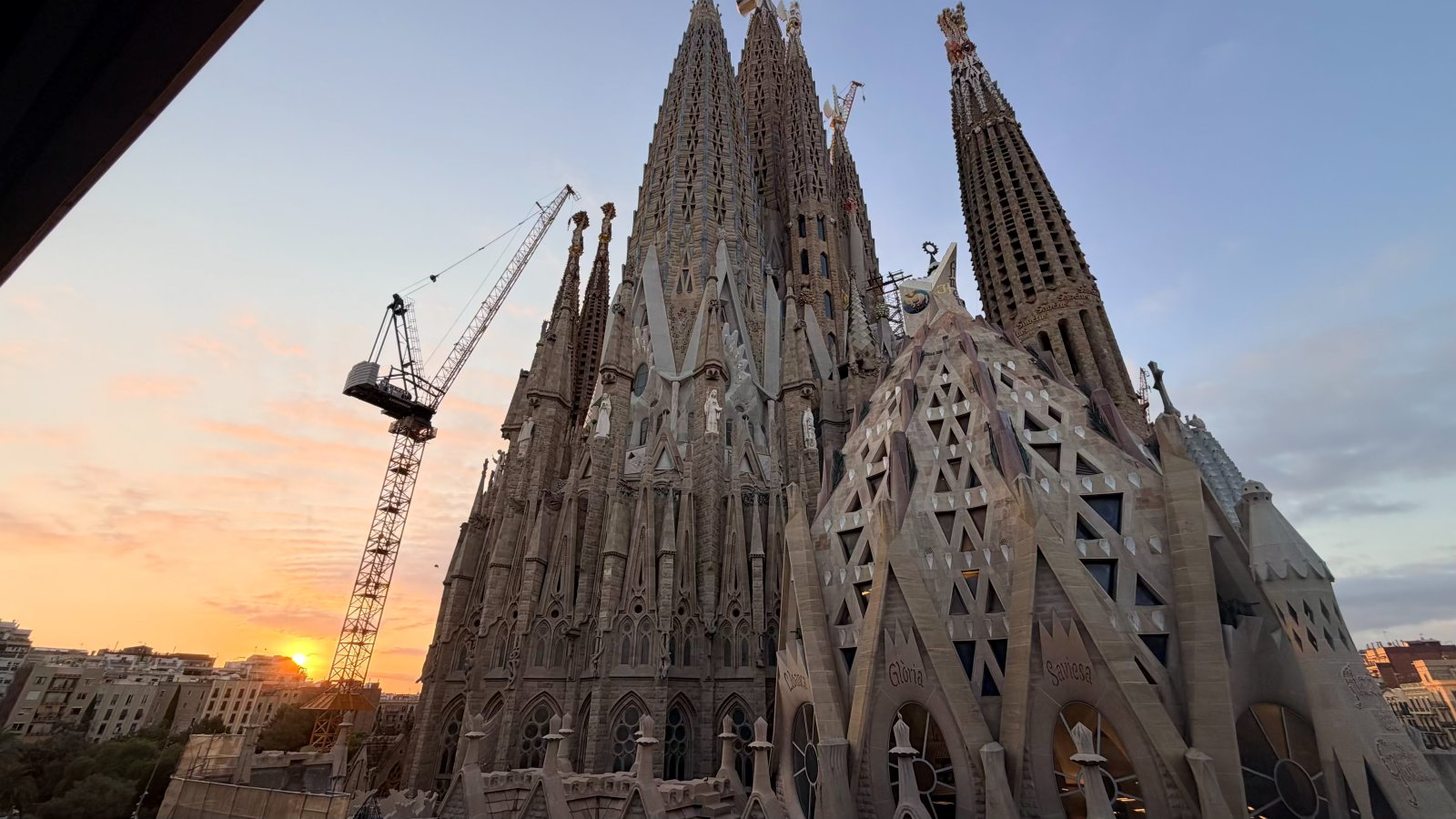 Full view of the Sagrada Familia at sunrise, pink and orange sky, seen from the apartment balcony