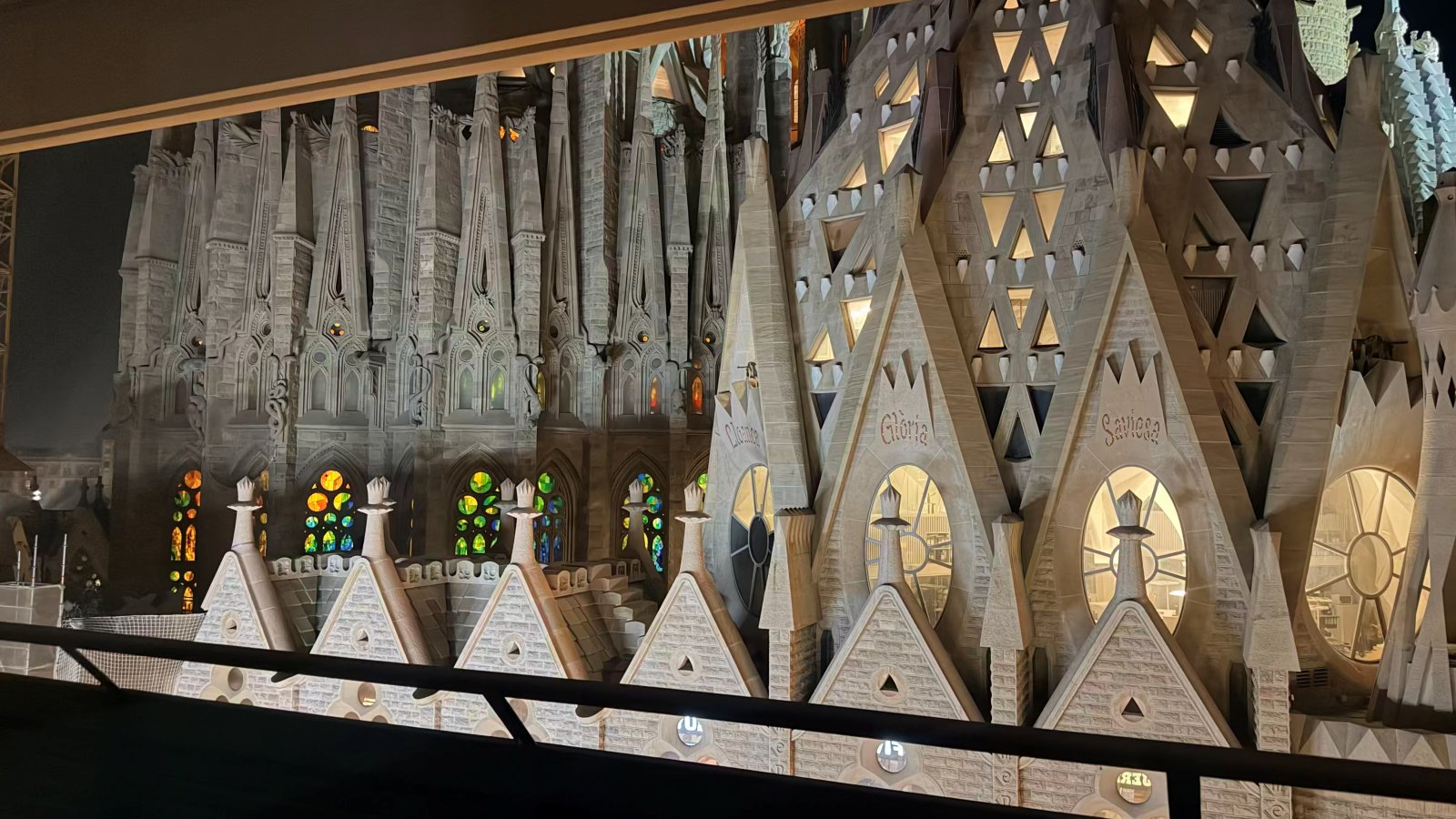 Sagrada Familia illuminated at night with glowing stained glass, seen from the balcony